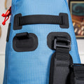 A Cancha Tennis Travel Bundle in blue with black buckles and red cord accents is featured on a white surface with a blurred background. It includes square and rectangular attachment points for the straps, making it an ideal travel accessory. Perfect as a Racquet Bag Voyager or adaptable wet-dry bag.