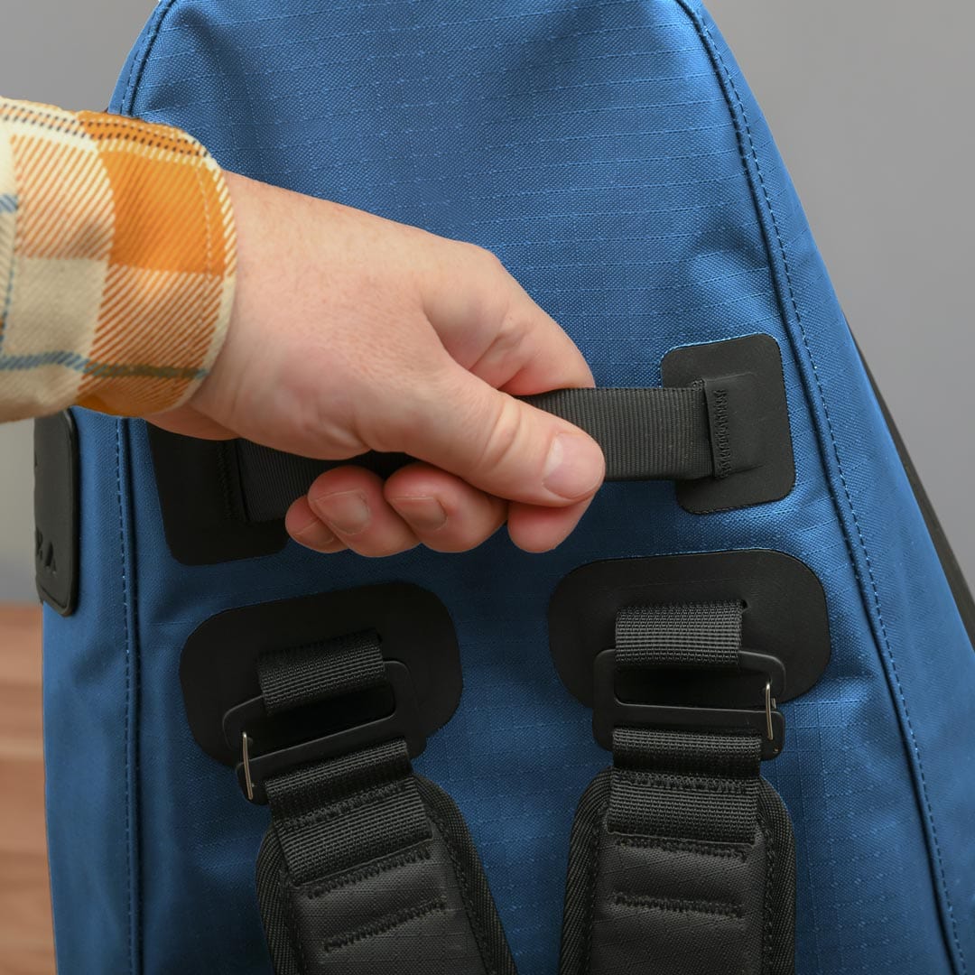 A hand adjusts the strap on the back of Cancha's Tennis Travel Bundle, designed to carry all your travel accessories. The person, dressed in a plaid shirt with hues of orange, yellow, and white, appears ready for an adventure.